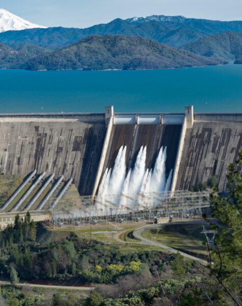 A picture of Shasta Dam surrounded by roads and trees with a lake and mountains on the background